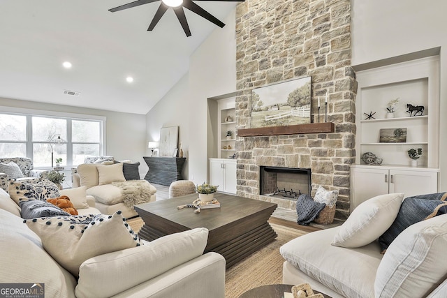 living room featuring built in shelves, a stone fireplace, wood finished floors, visible vents, and a ceiling fan