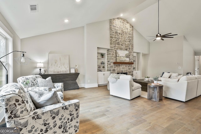 living area featuring high vaulted ceiling, light wood-style flooring, a fireplace, and visible vents