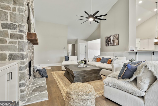 living room featuring ceiling fan, high vaulted ceiling, a fireplace, and wood finished floors