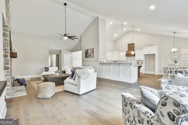 living area featuring high vaulted ceiling, light wood-style flooring, and ceiling fan with notable chandelier