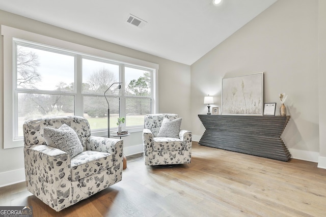 living area featuring vaulted ceiling, wood finished floors, visible vents, and baseboards