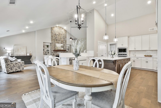 dining area with ceiling fan with notable chandelier, high vaulted ceiling, light wood-style flooring, and visible vents