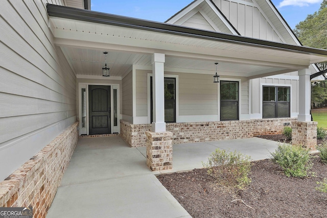 view of exterior entry featuring covered porch, brick siding, and board and batten siding