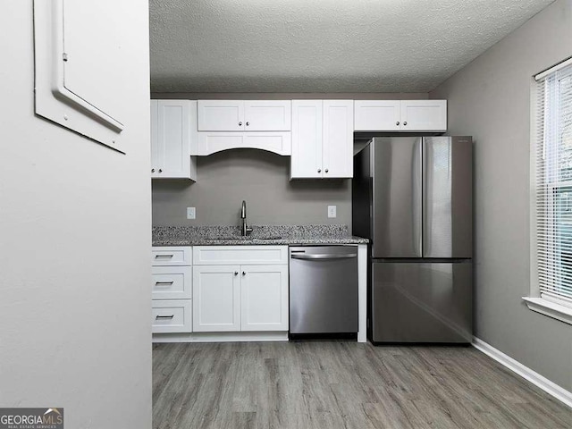 kitchen featuring stainless steel appliances, a healthy amount of sunlight, stone counters, white cabinetry, and a sink