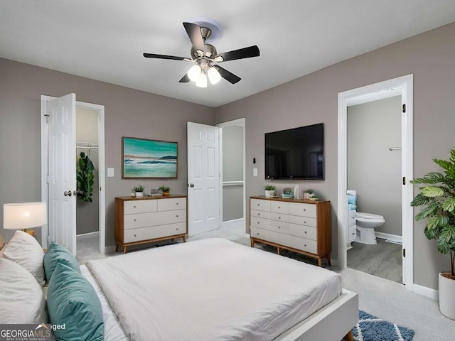 bedroom featuring baseboards, light colored carpet, ensuite bath, a walk in closet, and a closet