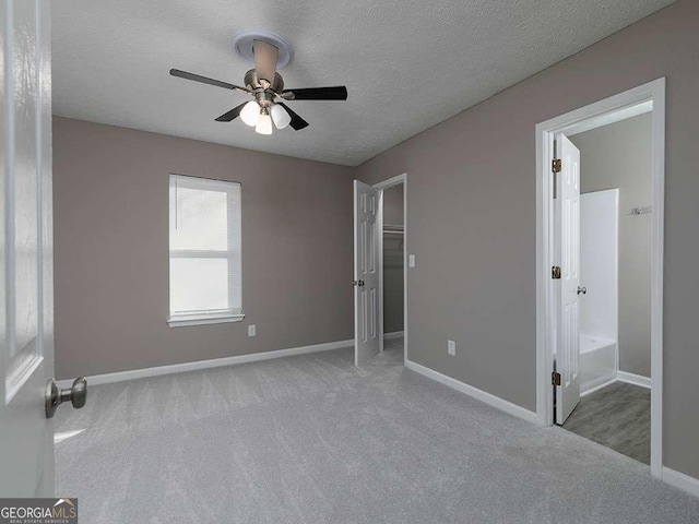 unfurnished bedroom featuring a textured ceiling, ensuite bathroom, a ceiling fan, baseboards, and carpet