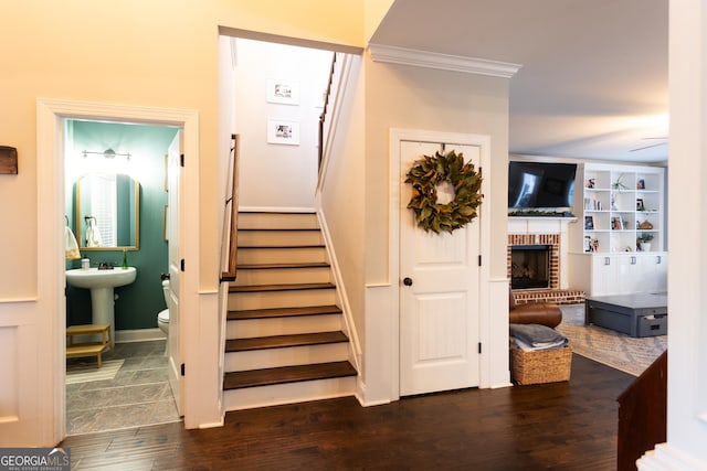 stairway featuring ceiling fan, a fireplace, wood finished floors, baseboards, and ornamental molding