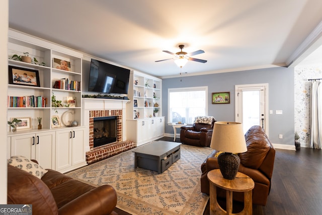 living area featuring crown molding, a ceiling fan, a brick fireplace, wood finished floors, and baseboards