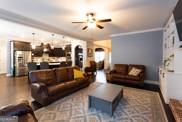 living room with arched walkways, dark wood-type flooring, a ceiling fan, baseboards, and ornamental molding