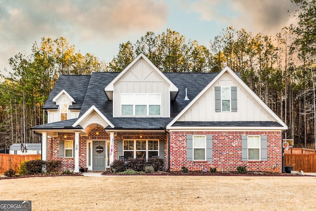 view of front facade with board and batten siding, a front yard, brick siding, and fence