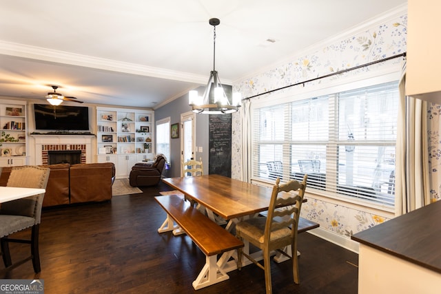 dining area featuring crown molding, dark wood finished floors, a fireplace, wallpapered walls, and ceiling fan with notable chandelier