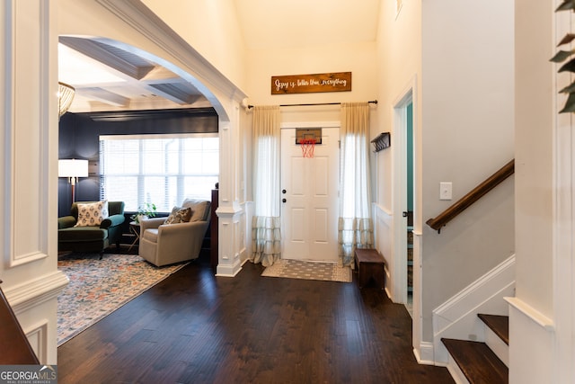 foyer entrance featuring arched walkways, coffered ceiling, wood finished floors, stairway, and beamed ceiling