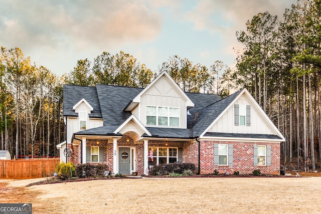 view of front of home featuring brick siding, fence, roof with shingles, board and batten siding, and a front yard