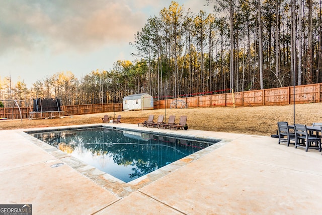 view of pool with a patio, a fenced backyard, an outdoor structure, a shed, and a trampoline