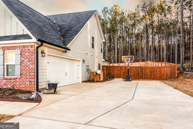 view of side of property featuring a shingled roof, concrete driveway, brick siding, and board and batten siding