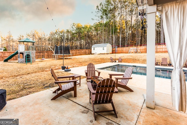 view of patio with a trampoline, an outbuilding, a playground, a storage shed, and a fenced backyard