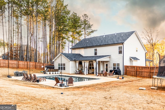 rear view of house featuring a trampoline, a fenced in pool, a fenced backyard, and a patio