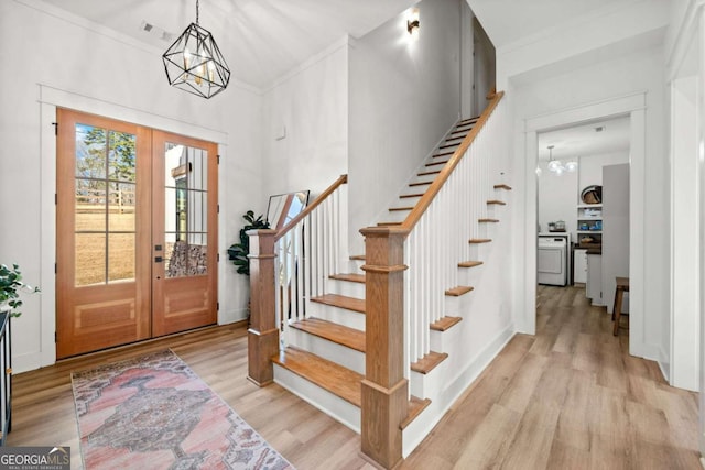 foyer featuring light wood finished floors, crown molding, a chandelier, stairway, and french doors