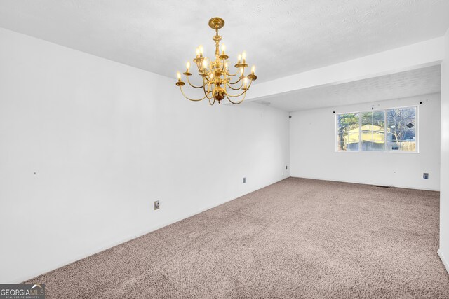 spare room featuring carpet floors, a notable chandelier, and a textured ceiling