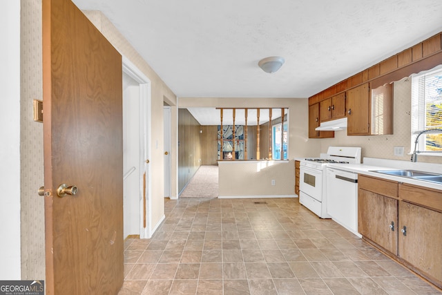 kitchen with white appliances, wallpapered walls, a sink, light countertops, and under cabinet range hood