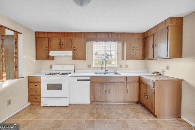 kitchen featuring under cabinet range hood, a sink, wallpapered walls, white appliances, and light countertops