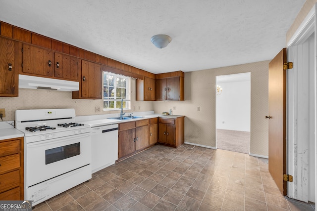 kitchen with white appliances, wallpapered walls, a sink, under cabinet range hood, and a textured ceiling