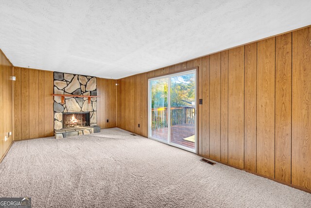 unfurnished living room with visible vents, carpet floors, a stone fireplace, and wood walls