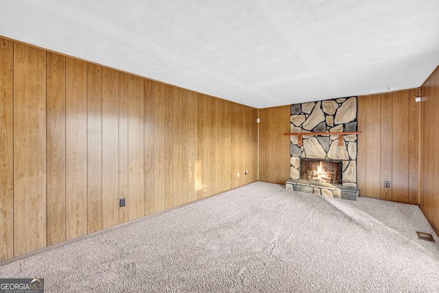 unfurnished living room featuring visible vents, wooden walls, a stone fireplace, and carpet