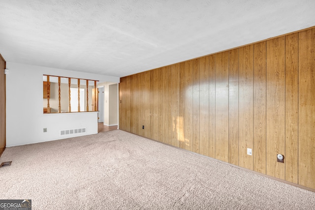 empty room featuring carpet flooring, visible vents, wood walls, and a textured ceiling