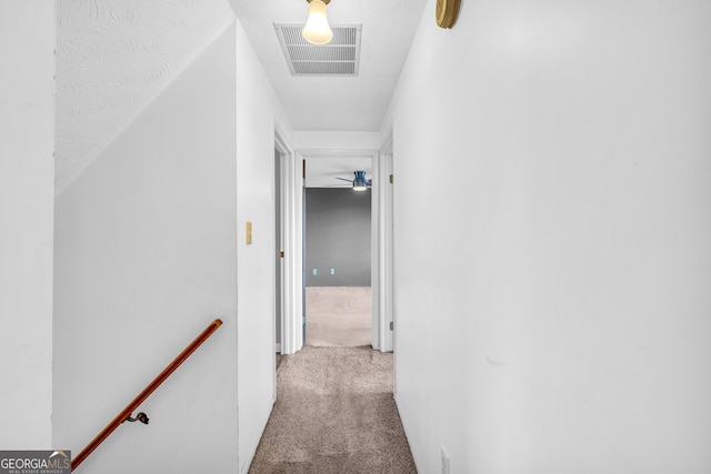 hallway featuring an upstairs landing, visible vents, and carpet