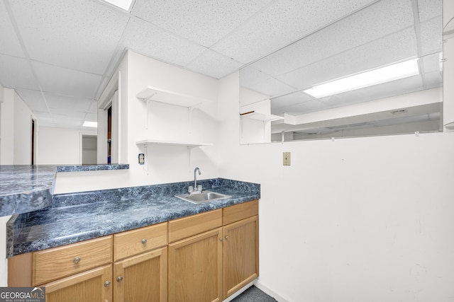 kitchen with open shelves, a paneled ceiling, dark countertops, and a sink