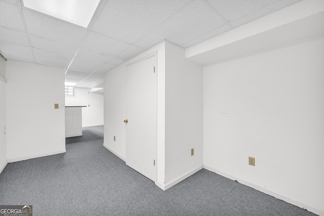 basement featuring a drop ceiling, baseboards, and carpet flooring