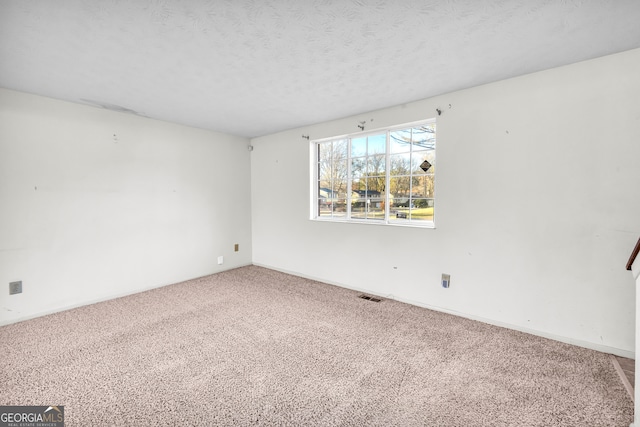 carpeted spare room featuring baseboards, visible vents, and a textured ceiling