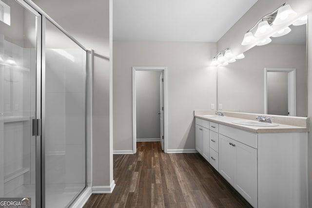 full bathroom with double vanity, a stall shower, baseboards, wood finished floors, and a sink