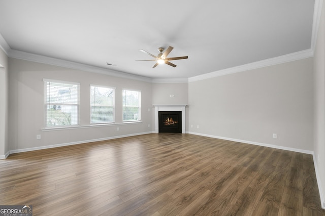unfurnished living room with a warm lit fireplace, baseboards, wood finished floors, and crown molding