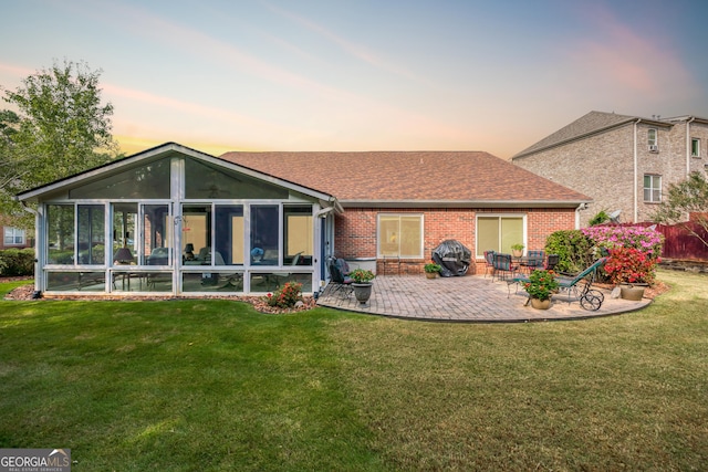 back of house featuring a patio, brick siding, a sunroom, a lawn, and roof with shingles