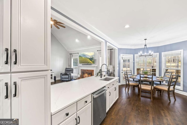 kitchen with lofted ceiling, a sink, white cabinetry, a lit fireplace, and stainless steel dishwasher