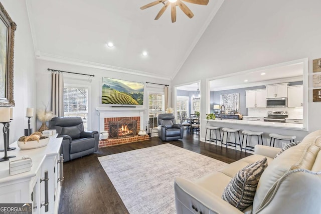 living room with dark wood-style floors, ceiling fan, crown molding, a brick fireplace, and high vaulted ceiling