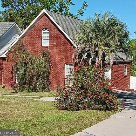 view of property exterior with brick siding, a lawn, and roof with shingles