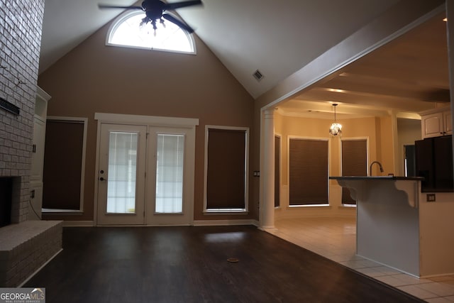 unfurnished living room featuring high vaulted ceiling, light wood-style flooring, ceiling fan with notable chandelier, visible vents, and a brick fireplace