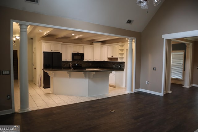 kitchen featuring light wood-type flooring, decorative columns, dark countertops, and black appliances