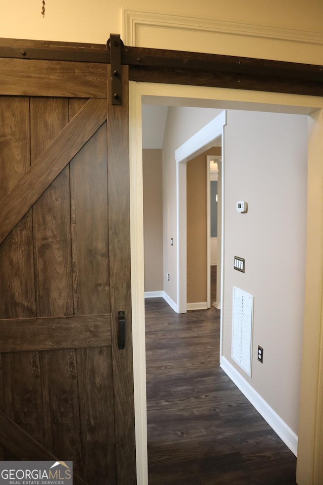 hall featuring baseboards, a barn door, visible vents, and dark wood-type flooring