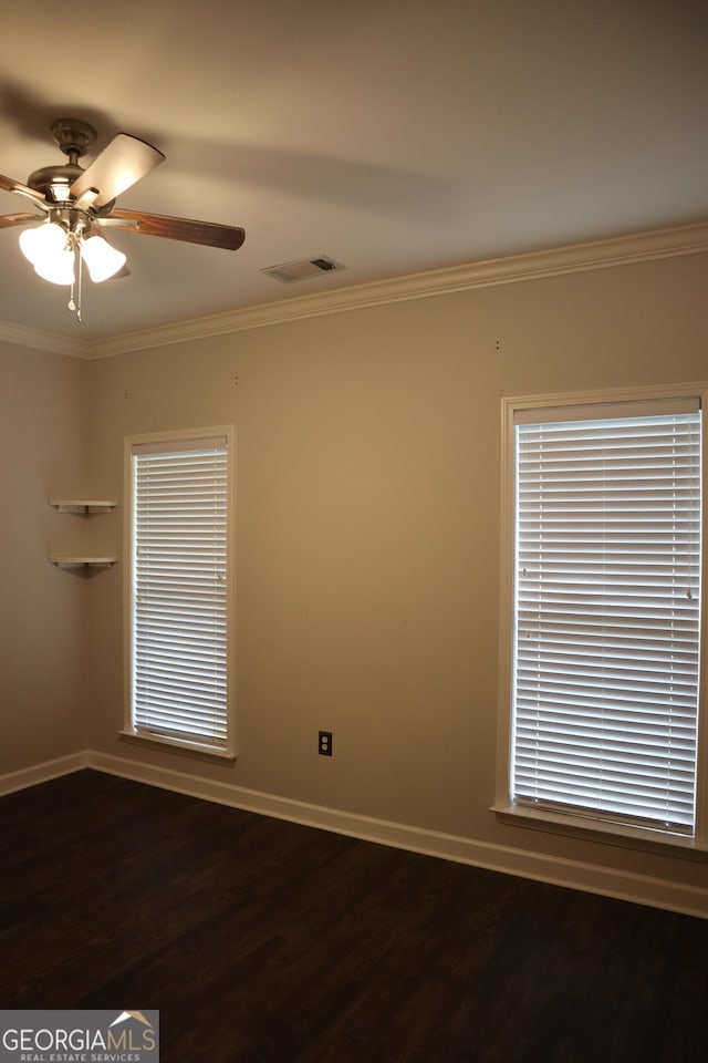 empty room featuring baseboards, dark wood-type flooring, visible vents, and crown molding