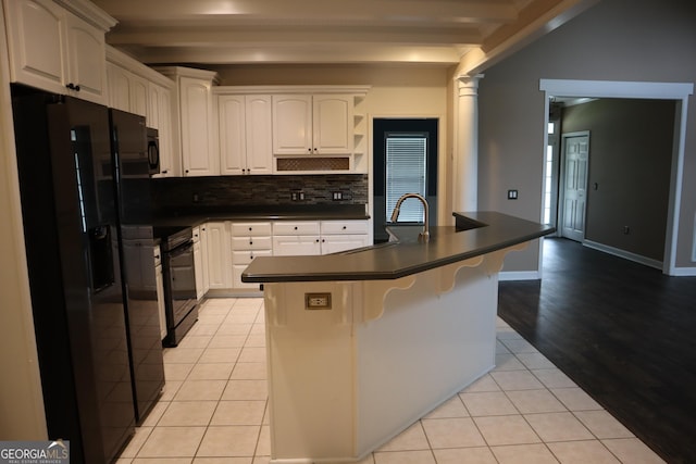 kitchen featuring light tile patterned floors, dark countertops, black appliances, decorative backsplash, and a sink