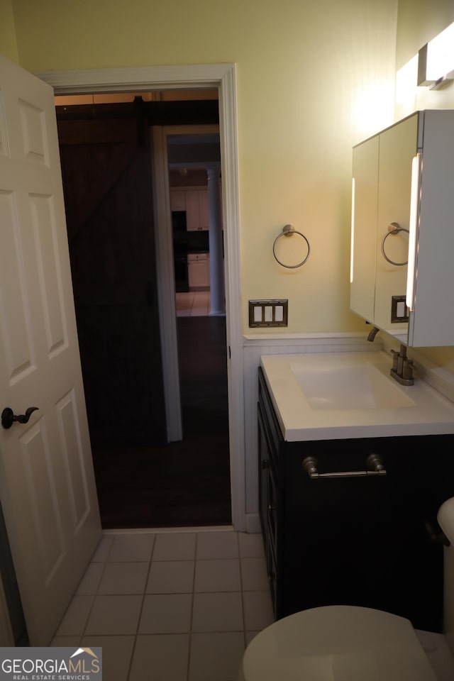 half bathroom with wainscoting, vanity, toilet, and tile patterned floors