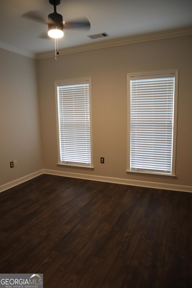 spare room featuring baseboards, visible vents, a ceiling fan, dark wood-style floors, and ornamental molding