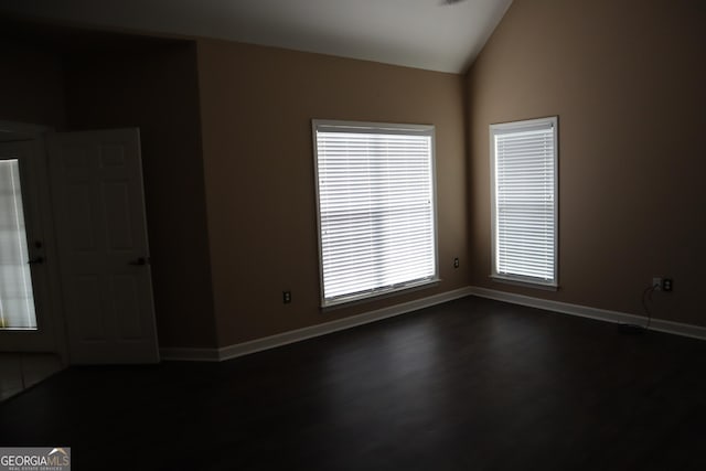 spare room with dark wood-type flooring, lofted ceiling, and baseboards