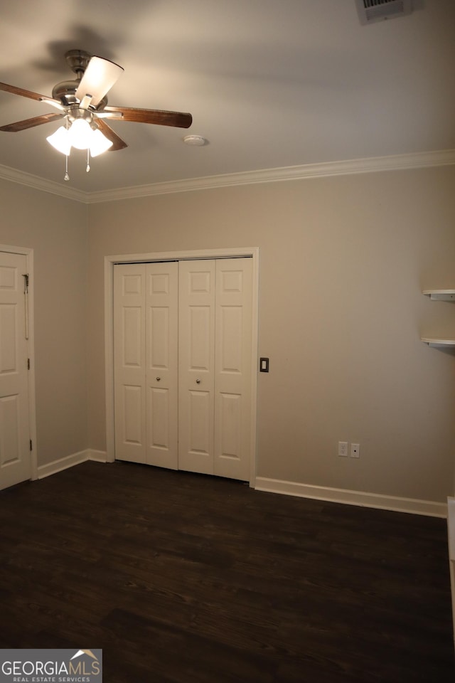 unfurnished bedroom with a closet, baseboards, ceiling fan, dark wood-style floors, and crown molding
