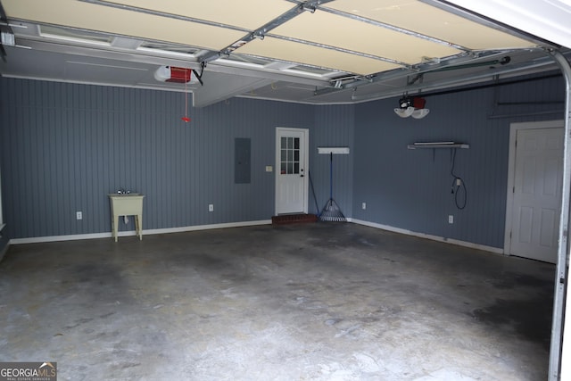 garage featuring a garage door opener, electric panel, a sink, and baseboards