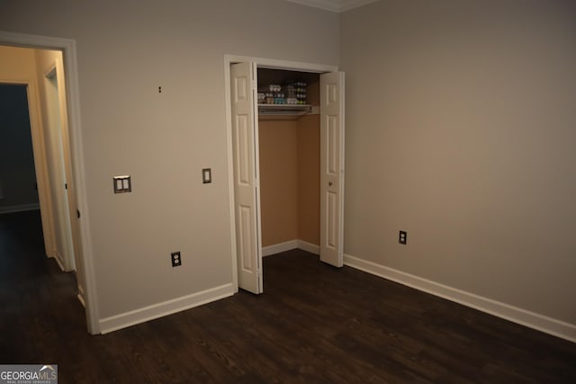 unfurnished bedroom with crown molding, a closet, baseboards, and dark wood finished floors